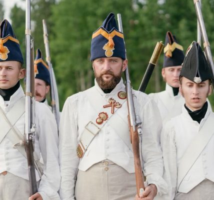 Soldiers marching in historical military uniforms reenact past events outdoors.