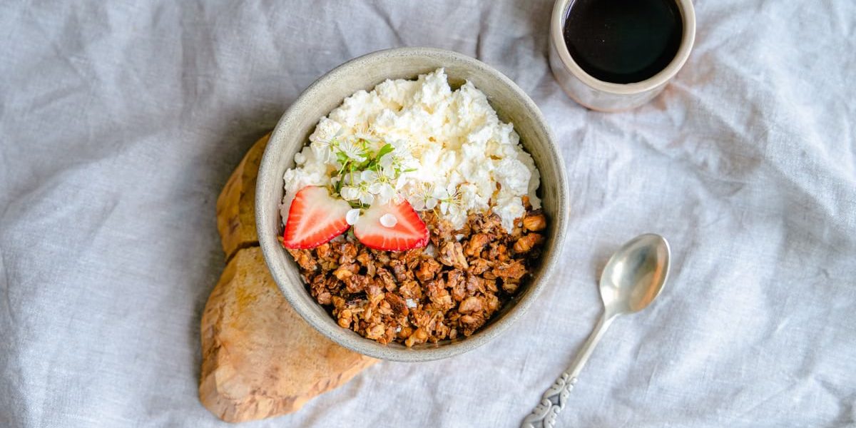 A delicious breakfast bowl with cottage cheese, granola, and strawberries served with black coffee.