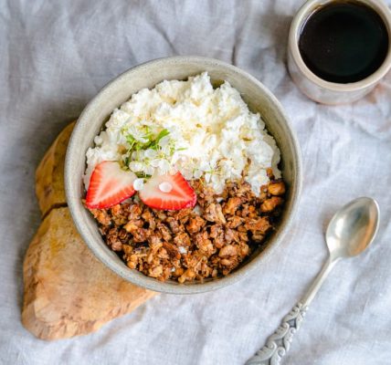 A delicious breakfast bowl with cottage cheese, granola, and strawberries served with black coffee.